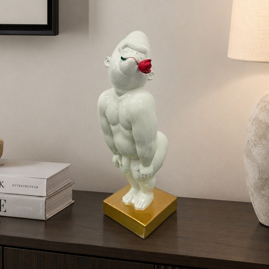 A glossy white gorilla figurine with a red rose in its mouth, standing on a gold square base on a dark wooden console table.